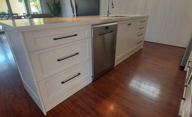 White kitchen island with timber flooring and integrated appliances